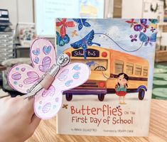 a hand holding up a book with a butterfly on the cover and an image of a school bus