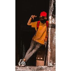 a man with a red hat and backpack leaning against a wall while pointing at something