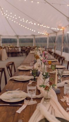 a long table set with plates and napkins under a tented area for dinner