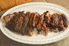 a white plate topped with sliced up meat on top of a wooden table next to a knife and fork