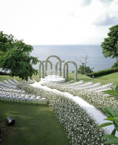 an outdoor ceremony setup with white chairs and flowers on the grass, overlooking the ocean