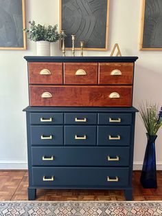 a blue dresser with gold handles and drawers in front of two pictures on the wall