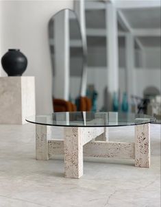 a glass table sitting on top of a white tiled floor next to a black vase