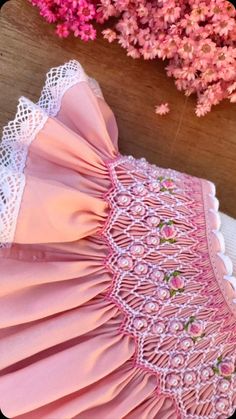 a pink dress with white lace on it and flowers in the backgroung