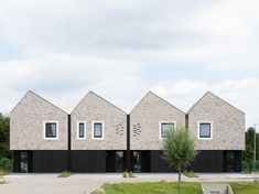 a row of black and white brick buildings with trees in the foreground on a cloudy day