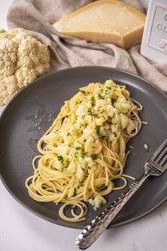 a plate with pasta and cheese on it next to a knife, fork and piece of bread