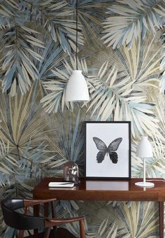 a table with two lamps and a framed photograph on it in front of a palm leaf wallpaper