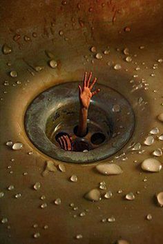 a person reaching up into a sink with water droplets on the floor and in the drain