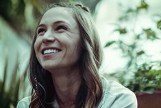 a smiling woman with long hair sitting in front of potted plants and looking up at the sky