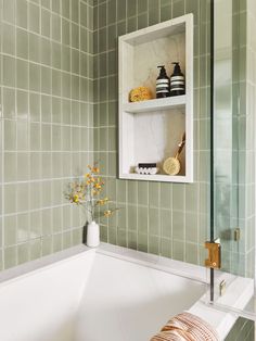 a white bath tub sitting next to a green tiled bathroom wall with shelves above it