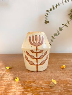 a ceramic vase sitting on top of a wooden table next to yellow flowers and greenery