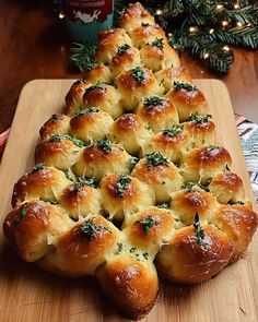 a wooden cutting board topped with rolls covered in cheese and herbs next to a christmas tree