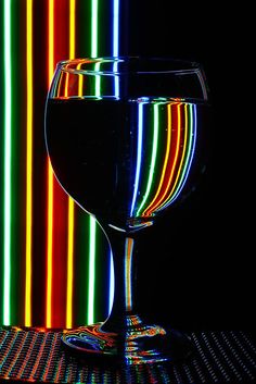 a glass of wine sitting on top of a table next to a neon striped wall