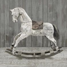 a white rocking horse with saddle on it's back and wooden planks in the background