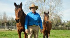 a man standing next to two horses in a field