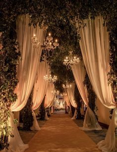 an aisle decorated with white draping and chandeliers is lit up at night