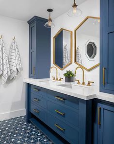 a bathroom with blue cabinets and white counter tops, two mirrors on the wall and gold accents