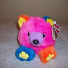 a pink and blue teddy bear sitting on top of a white tablecloth covered floor