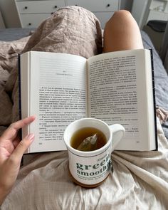 a person laying in bed with an open book and cup of tea on their lap