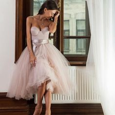 a woman standing in front of a window talking on a cell phone wearing a pink dress