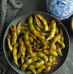 green beans are in a bowl on a table next to a blue and white dish