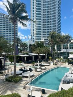 an outdoor swimming pool with lounge chairs and palm trees in front of high rise buildings