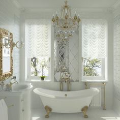 a white bathroom with gold accents and chandelier above the bathtub in front of two windows