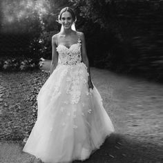 a woman in a wedding dress standing on the side of a road with trees behind her