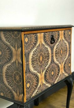 an ornate wooden cabinet with black and gold paint on the front, sitting on a hard wood floor