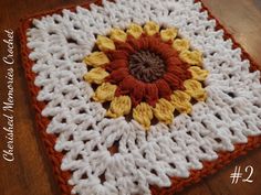 an orange and white crocheted square with a flower in the center on a wooden surface