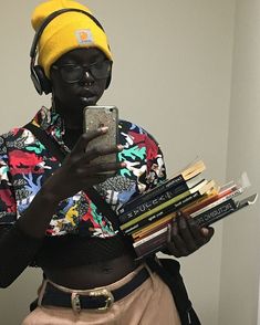 a woman wearing headphones and looking at her cell phone while holding books in front of her