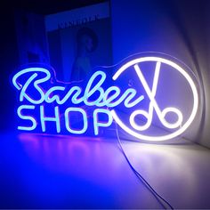 a neon sign that says barber shop with scissors in the center and blue light behind it