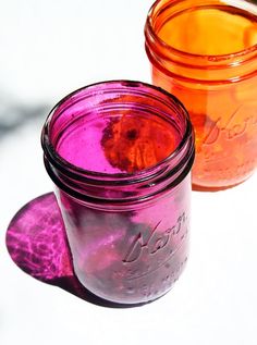 two jars filled with different colored liquid sitting on top of a white table next to each other