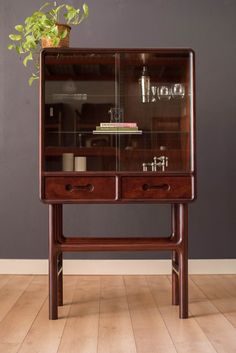 a wooden cabinet with glass doors and drawers on it's sides, in front of a gray wall