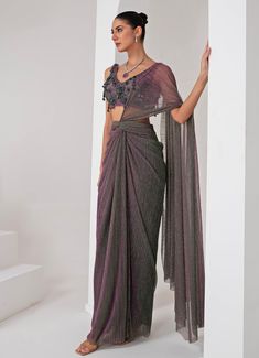 Elevate your style with the exquisite Lavender Pre Draped Crepe Saree, meticulously crafted from a luxurious platinoir crepe. The lavender saree shimmers with a subtle metallic tone, adding a touch of contemporary elegance to the traditional silhouette. Paired with a sleeveless V-neck blouse, this ensemble showcases intricate tonal crystal tassel and cutdana embellishments, creating a perfect blend of modern flair and classic grace. The pre-draped design ensures effortless wear, making it an ideal choice for those who desire both sophistication and convenience. Whether you're attending a Cocktails, Sangeet nights or a glamorous evening event, this saree promises to make a statement, reflecting your impeccable taste and style. Composition : Blouse - Crepe blend, Saree - Platinoir Crepe Care Drape Saree Designer, Drape Saree Indo Western, Modern Saree Draping, Lavender Saree, Draped Saree, Saree Draping Styles, Modern Saree, Crepe Saree, Drape Saree