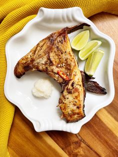 grilled fish on a white plate with lemon wedges and mashed potatoes next to it