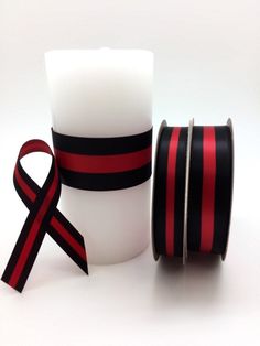 red and black ribbon sitting next to a white cup with a candle in it on a white surface