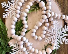 a wreath made out of white beads and snowflakes on top of a wood slice