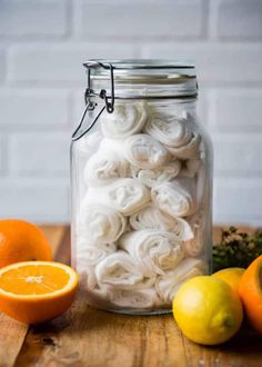 a jar filled with rolled up white towels next to oranges and lemons on a wooden table