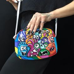 a woman's hand holding a brightly colored purse with monster faces on the front