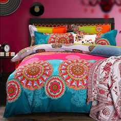 a bed with colorful comforters and pillows in a pink walled room, along with decorative wall hangings