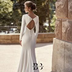 a woman in a long white dress is standing near a stone wall and looking off into the distance