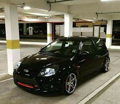 a small black car parked in a parking garage with yellow and white stripes on the floor