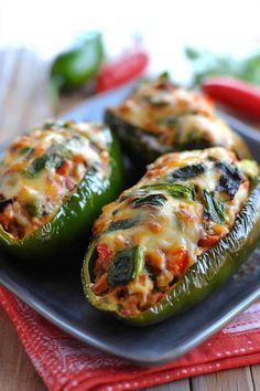 three stuffed peppers are on a plate with red napkins and green peppers in the background