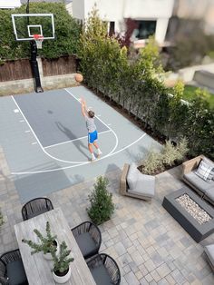 an aerial view of a man playing basketball on a backyard court with seating and tables