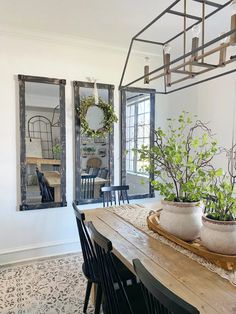 a dining room table with two potted plants on it and mirrors in the background