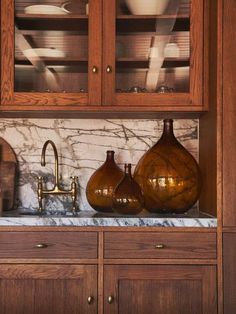 two brown vases sitting on top of a counter next to a wooden cabinet filled with dishes