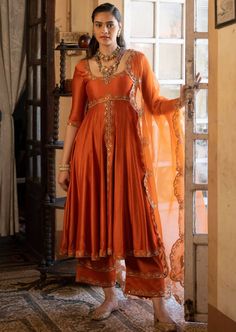 Featuring a rust chiniya silk anarkali set paired with tissue base dupatta with antique gold zari resham embroidery. Elegant Anarkali Suits, Ethnic Anarkali Dresses, Tissue Anarkali Dress, Embroidery On Orange Fabric, Tissue Fabric Dress Design, Silk Dresses Indian, Rust Orange Lehenga, Mehndi Gharara, Wedding Guests Outfits