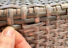 a hand is touching the side of a woven basket with wood strips on it's sides