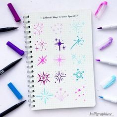 a spiral notebook with different colored stars and snowflakes on the cover, surrounded by markers